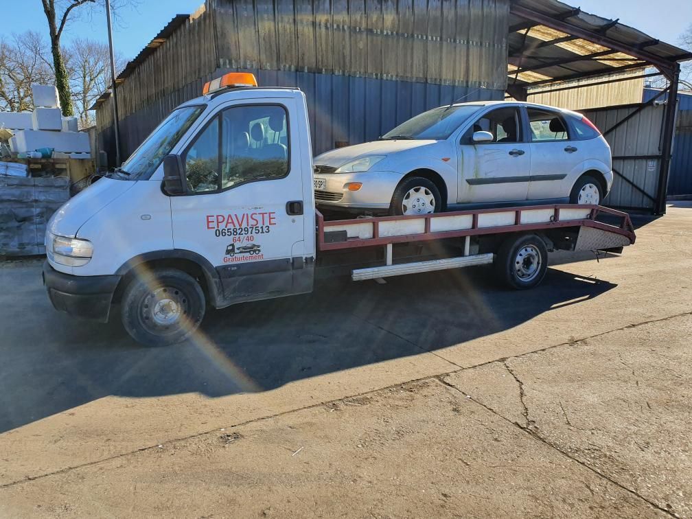 Dépanneuse transportant une voiture blanche devant un hangar métallique par une journée ensoleillée