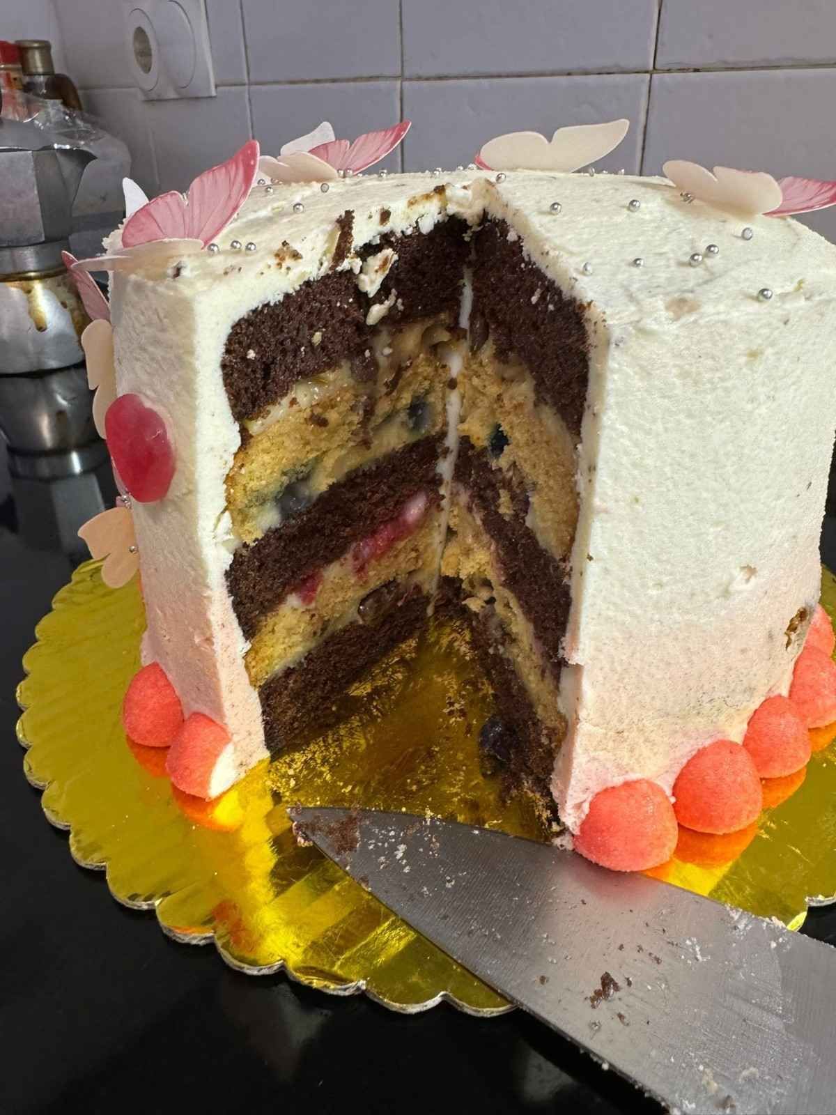 Un pastel de capas porcionado con capas alternas de bizcocho de chocolate y vainilla, glaseado blanco y mariposas de azúcar decorativas.