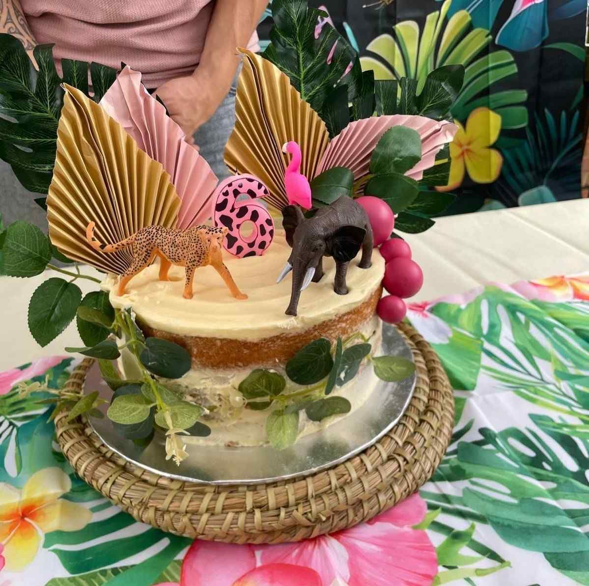 Una tarta de cumpleaños con temática de la selva para un niño de seis años, decorada con animales de juguete, hojas en forma de abanico y vegetación tropical.