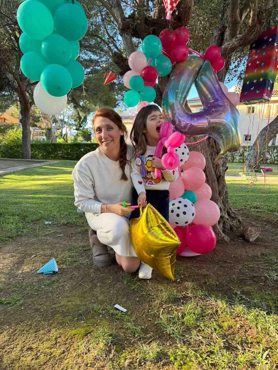 Una persona y un niño posaron al aire libre con numerosos globos de colores y un gran globo iridiscente con el número cuatro.