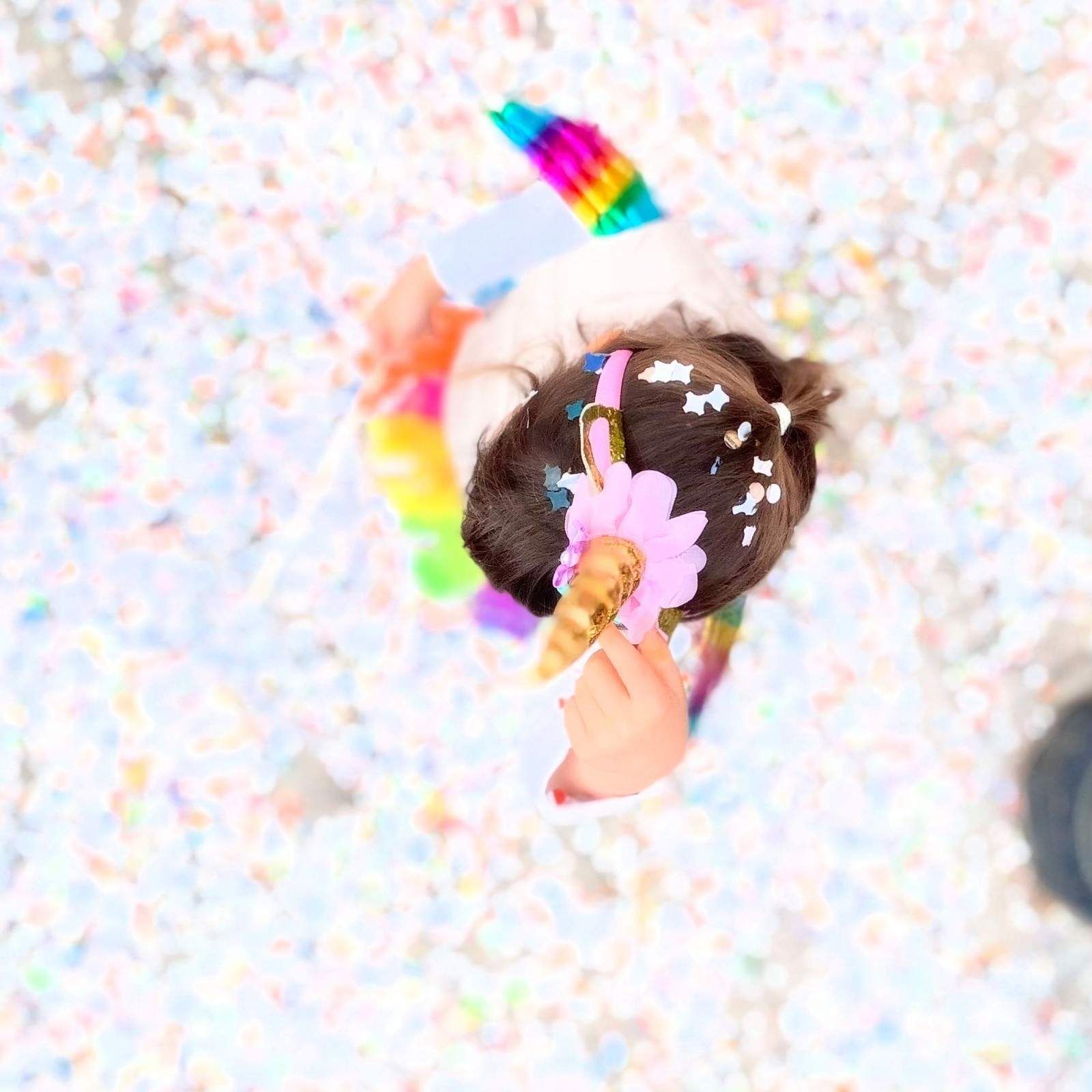 Vista desde arriba de una persona que lleva una diadema de unicornio con un cuerno dorado y una flor rosa, rodeada de confeti de colores.