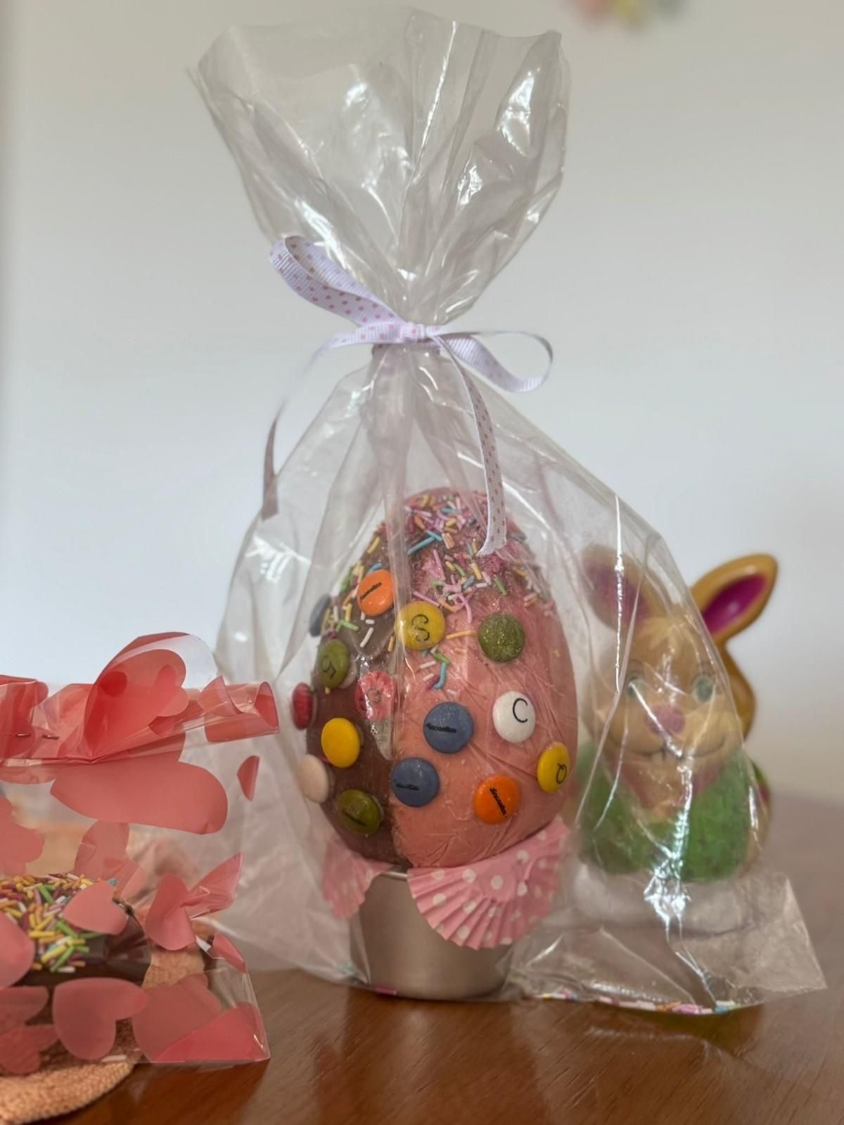 Un huevo de Pascua envuelto y decorado con botones de colores y confeti, junto a una pequeña figurita de conejito de cerámica.