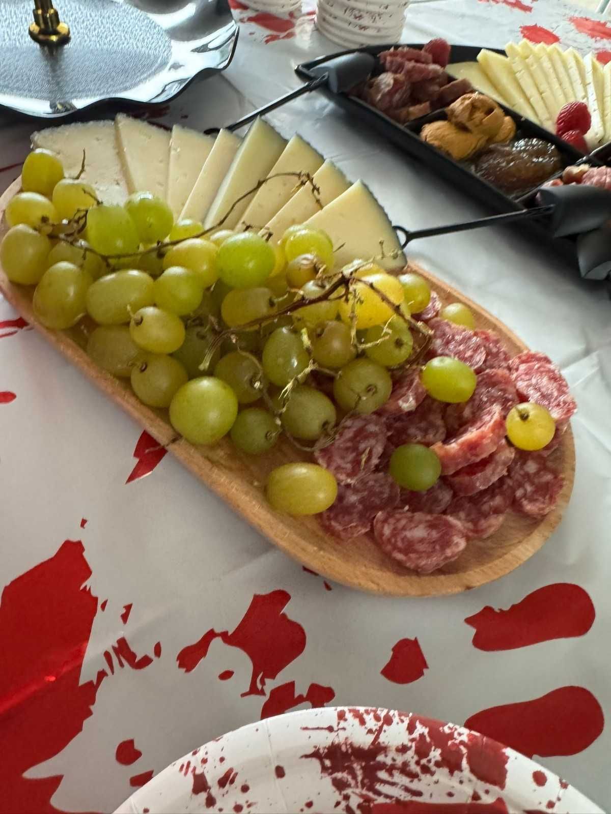 Una bandeja con lonchas de queso, uvas verdes y salami sobre una mesa con un mantel estampado en blanco y rojo.