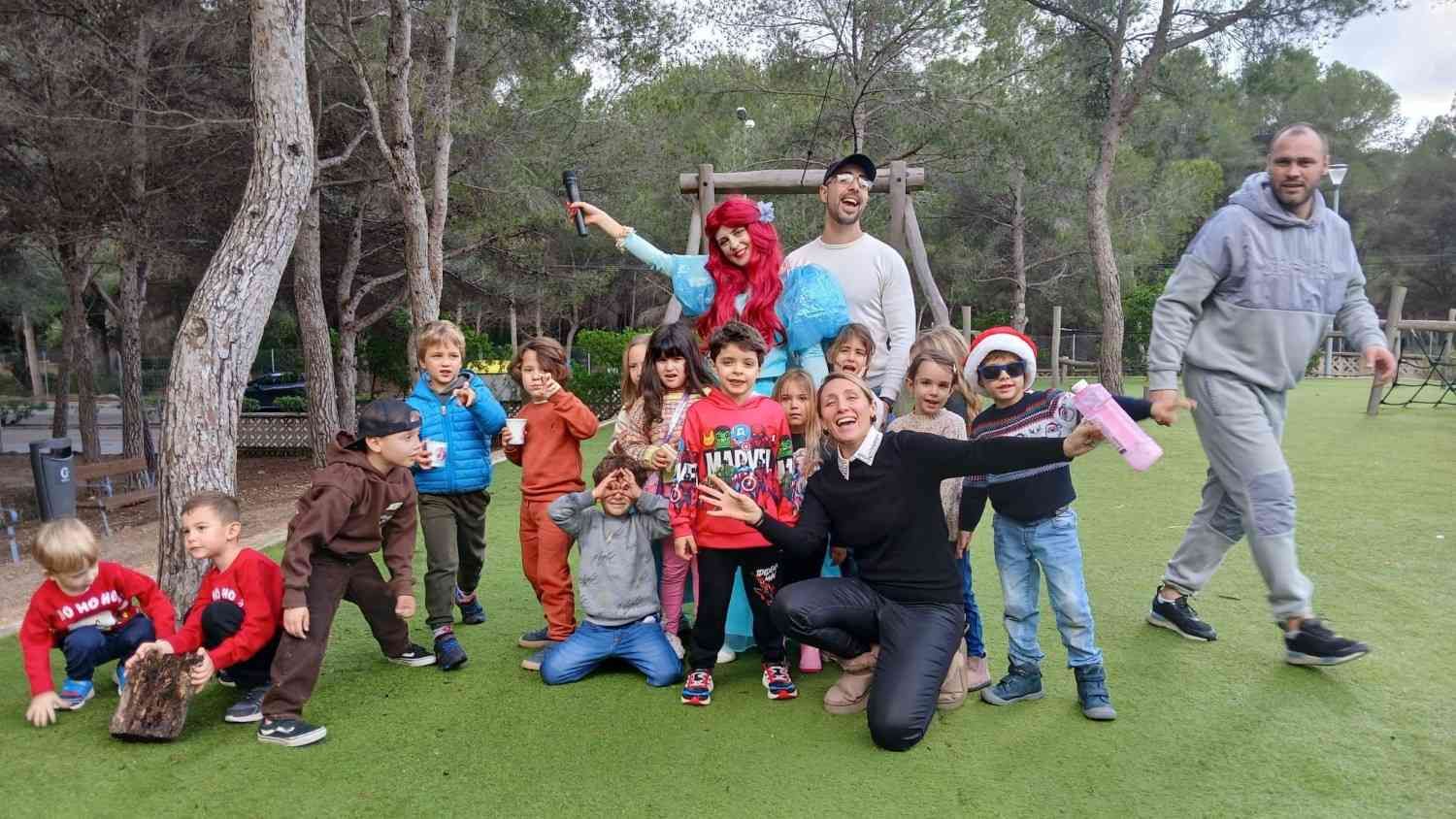 Un grupo de niños y adultos posando juntos en una zona de césped en un parque arbolado.
