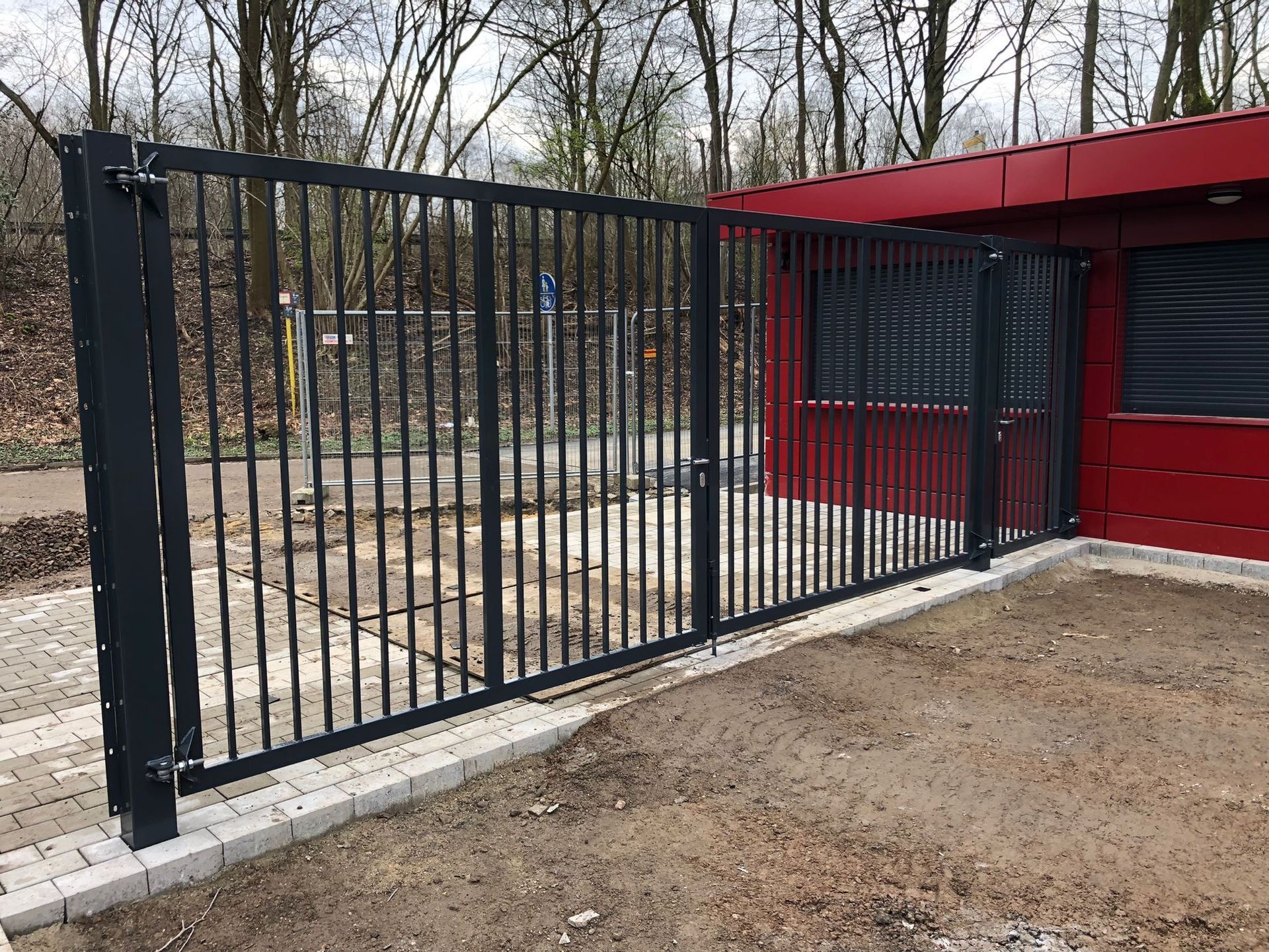 Vor einem roten Gebäude steht ein schwarzes Tor.