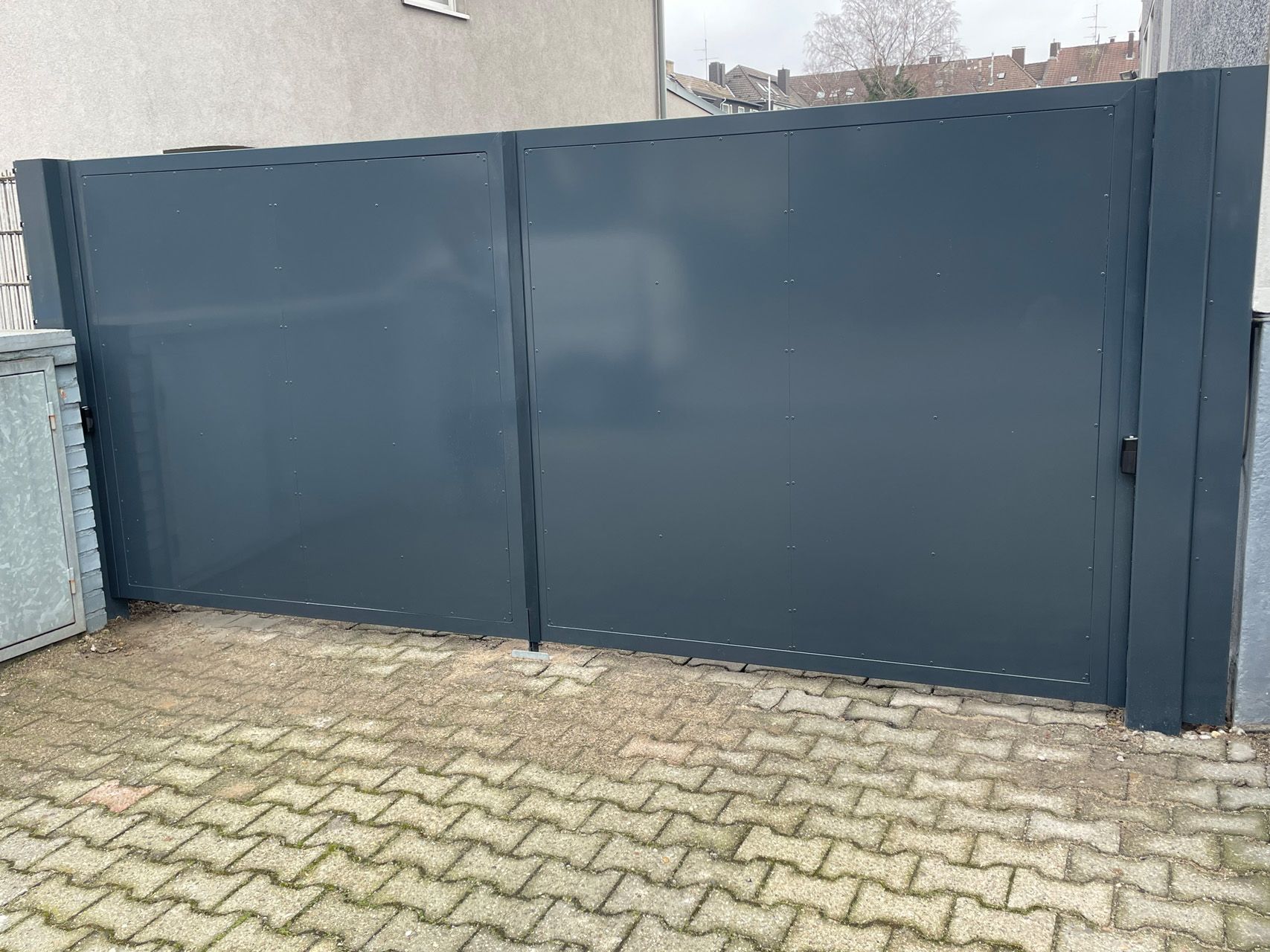 Ein Zaun umgibt eine gepflasterte Auffahrt vor einem Gebäude.