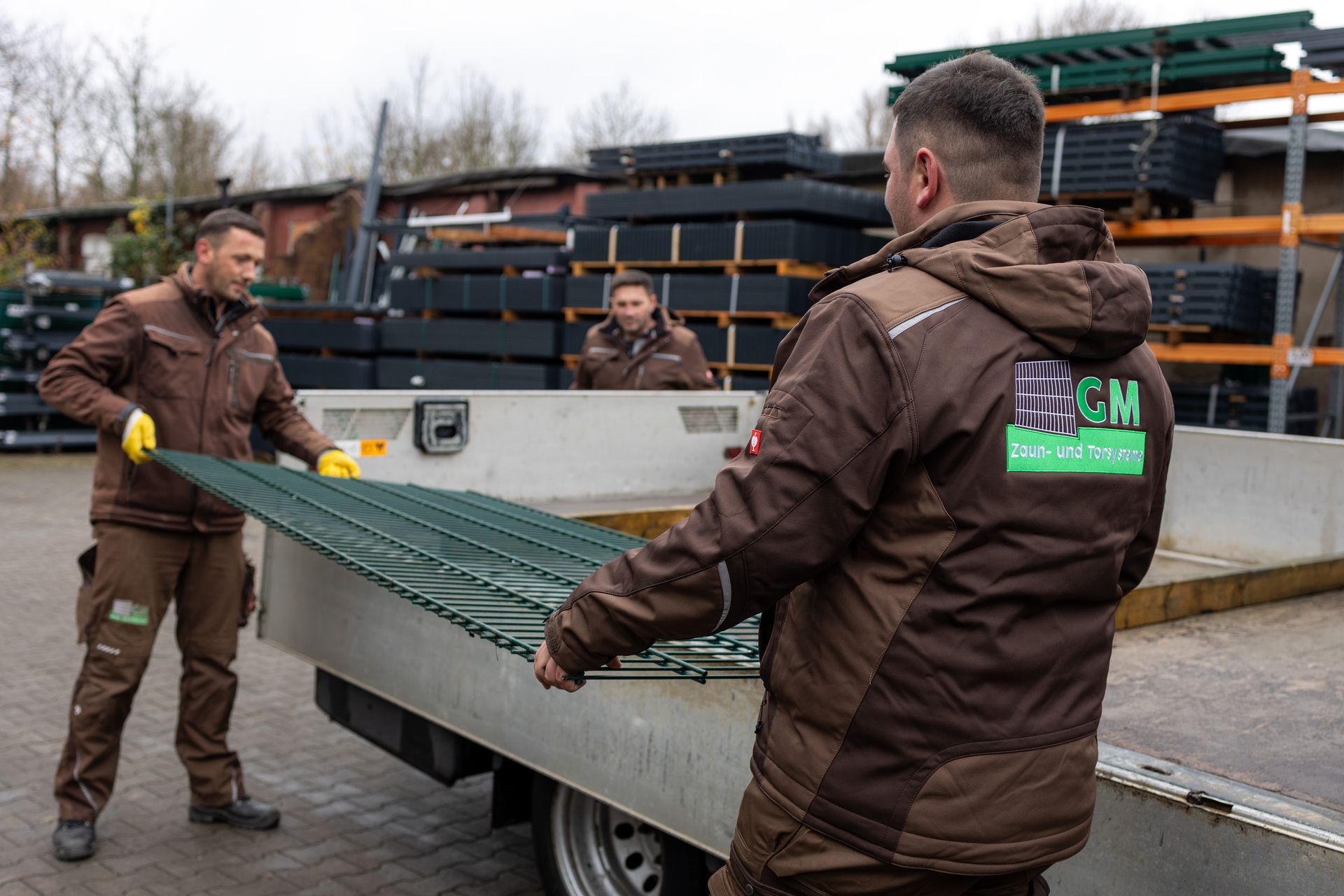 Zwei Männer beladen einen Anhänger mit einem grünen Zaun.
