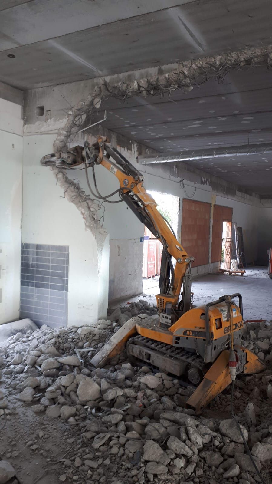 Ein gelber Bagger bricht eine Wand in einem Gebäude auf.