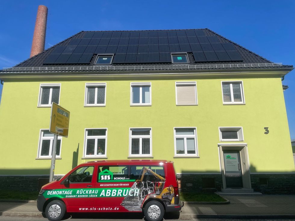 Ein roter Lieferwagen steht vor einem gelben Gebäude mit Solarmodulen auf dem Dach