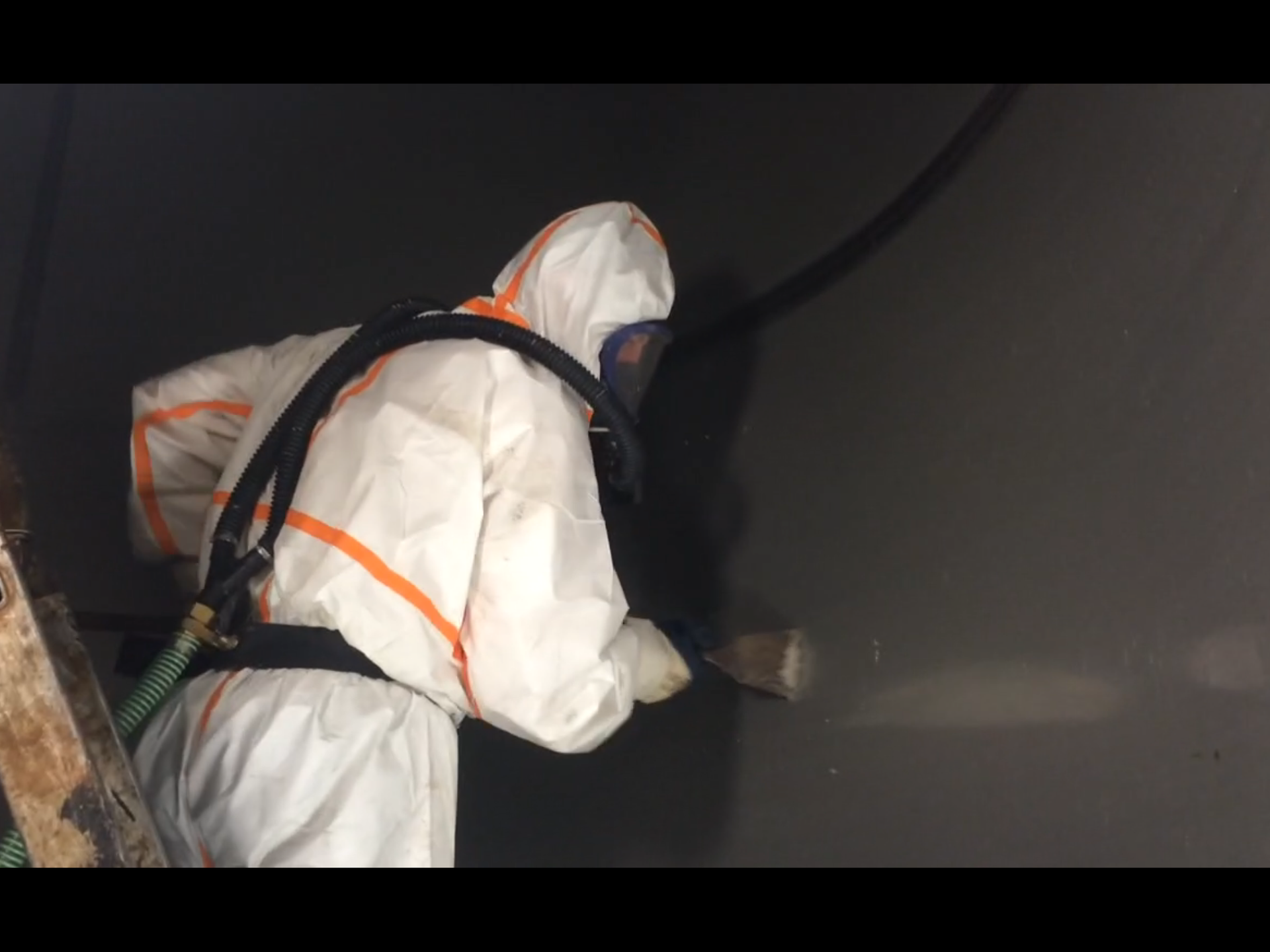 Ein Mann im Schutzanzug spritzt mit einem Schlauch eine Wand ab.