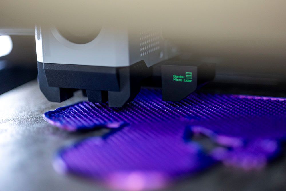 Ein 3D-Druckkopf druckt ein violettes Objekt auf eine ebene Fläche.