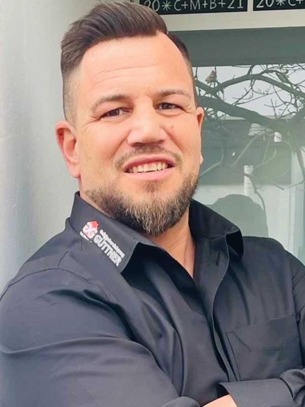 Ein Mann mit Bart trägt ein schwarzes Hemd und lächelt.