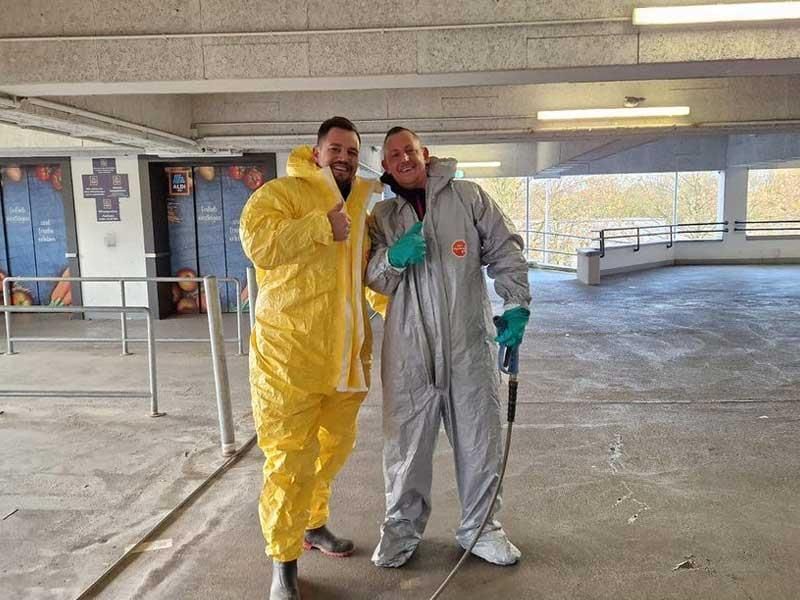 Zwei Männer in Schutzanzügen stehen nebeneinander in einem Parkhaus.