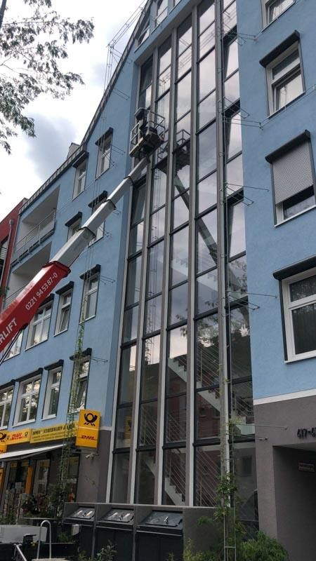 Ein Mann reinigt mit einem Kran die Fenster eines Gebäudes.