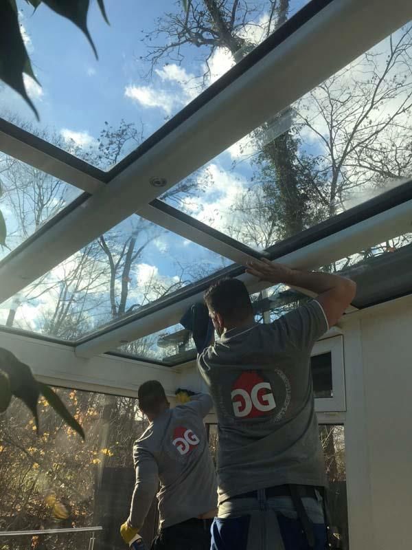 Zwei Männer arbeiten an einem Glasdach mit den Buchstaben GG auf ihren Hemden