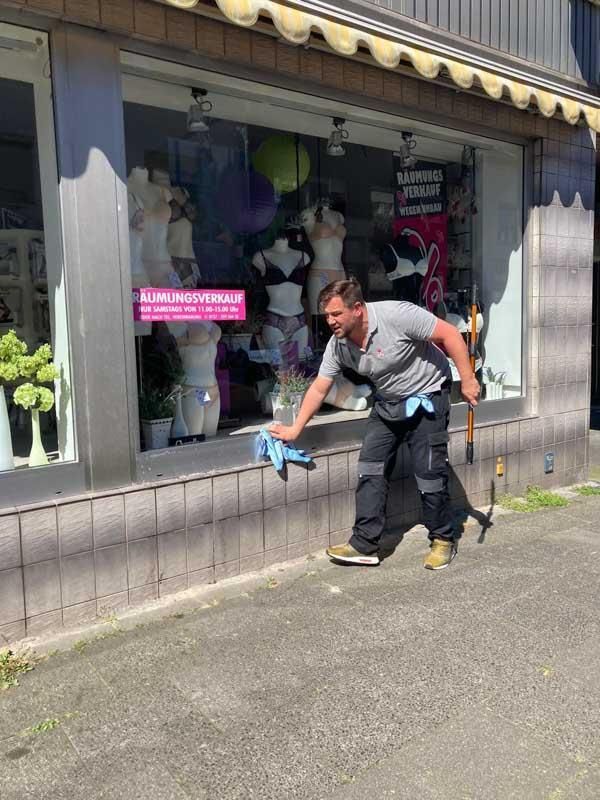 Ein Mann putzt mit einem Wischmopp ein Schaufenster.