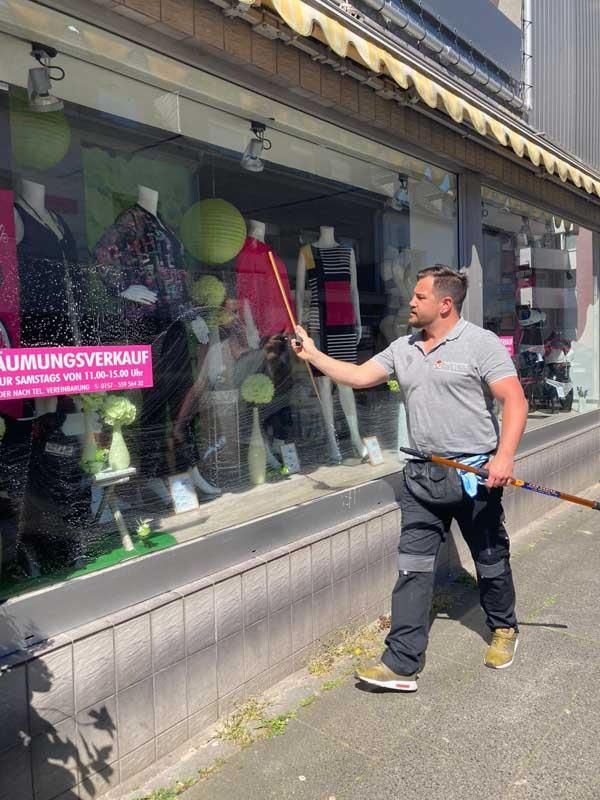 Ein Mann reinigt ein Schaufenster mit einem Schlauch.