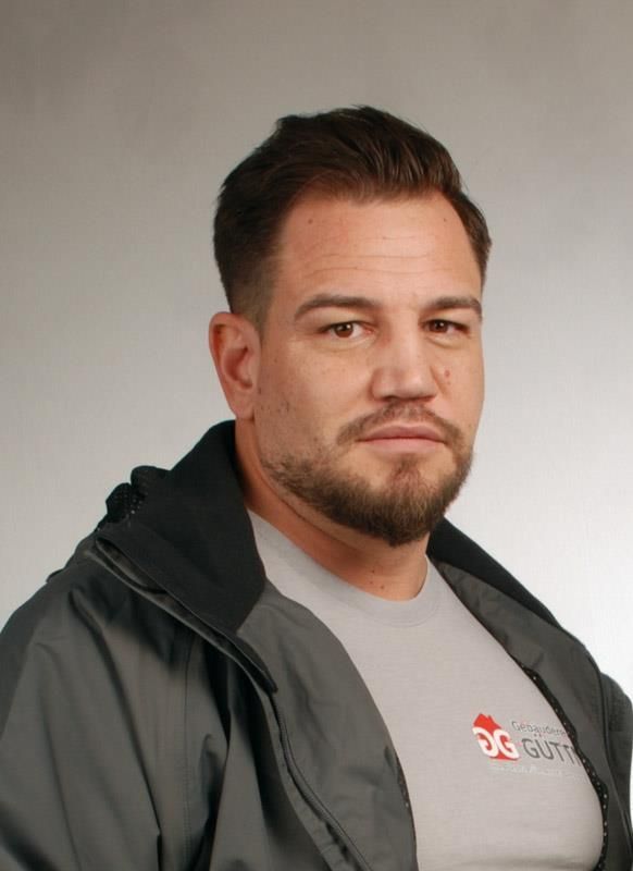 Ein Mann mit Bart trägt eine graue Jacke