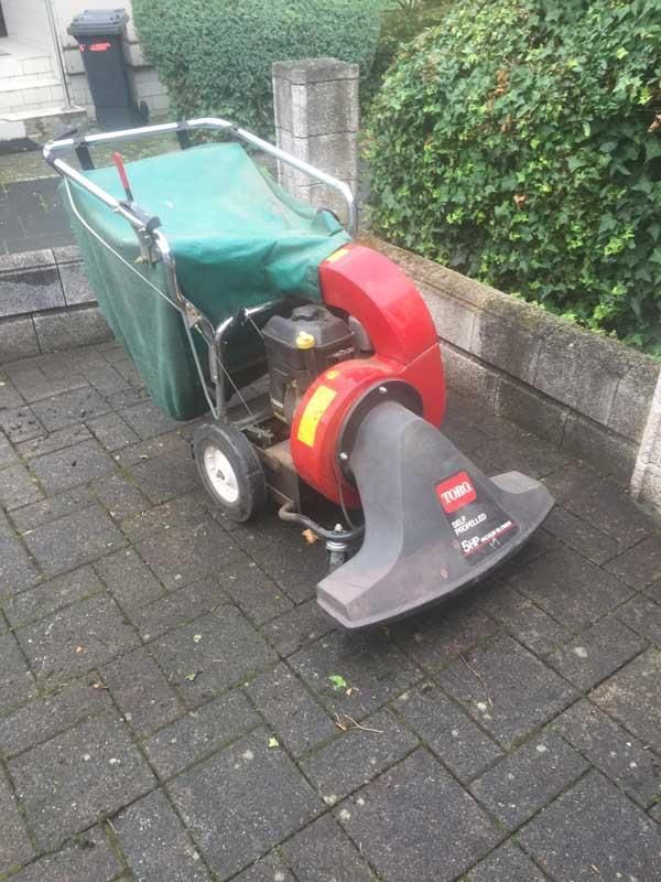 Ein rot-schwarzer Rasenmäher steht auf einem gepflasterten Gehweg.