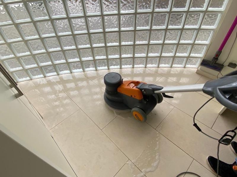 Eine Person reinigt einen Fliesenboden mit einer Maschine.