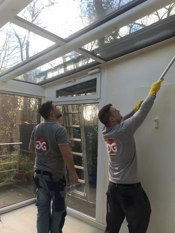Zwei Männer reinigen ein Glasdach in einem Wintergarten.