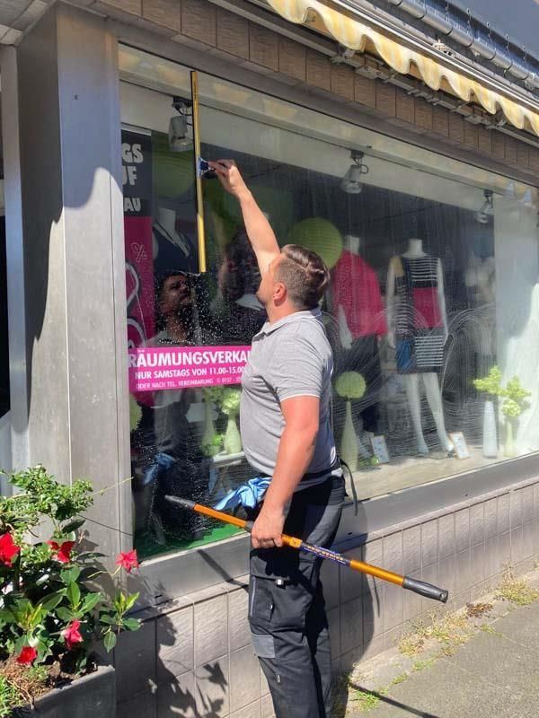 Ein Mann putzt mit einem Besen ein Schaufenster.