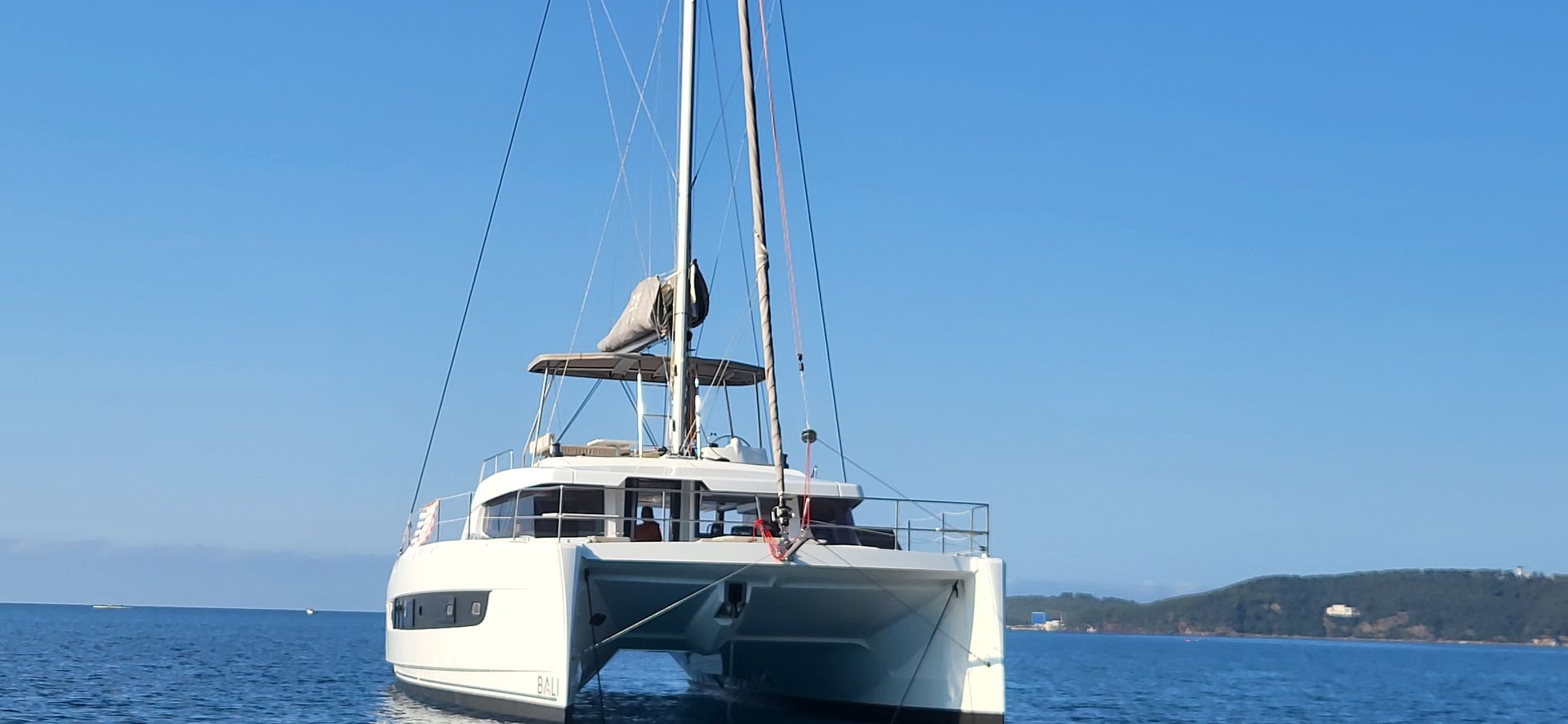 Un catamaran blanc naviguant sur une eau bleue sous un ciel d'un bleu clair et lumineux.