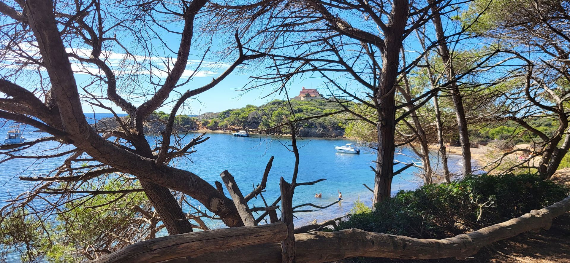 Vue d'une baie calme, bordée d'arbres. Une petite barque repose sur l'eau. Ciel d'un bleu éclatant.