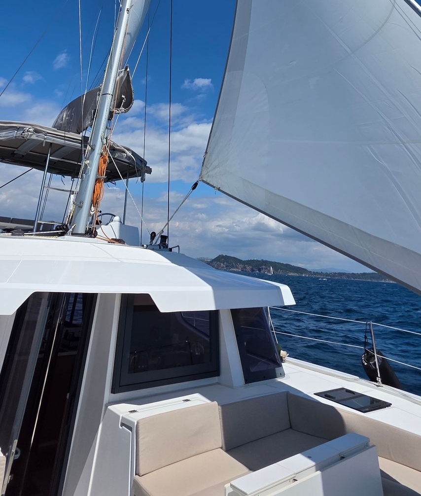 Voilier sur l'océan, voiles blanches gonflées, ciel et eau bleus, soleil éclatant.