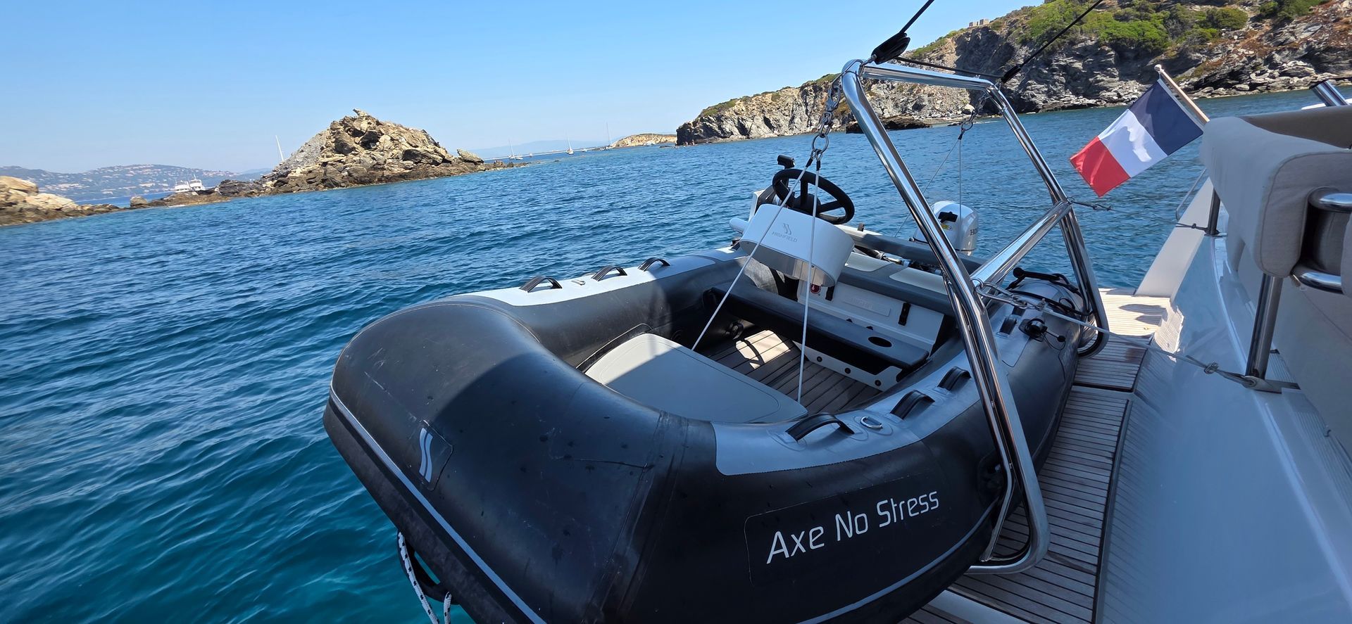 Un canot pneumatique sur le pont d'un bateau, arborant un drapeau français ; la mer et des îles rocheuses se dessinent à l'arrière-plan.