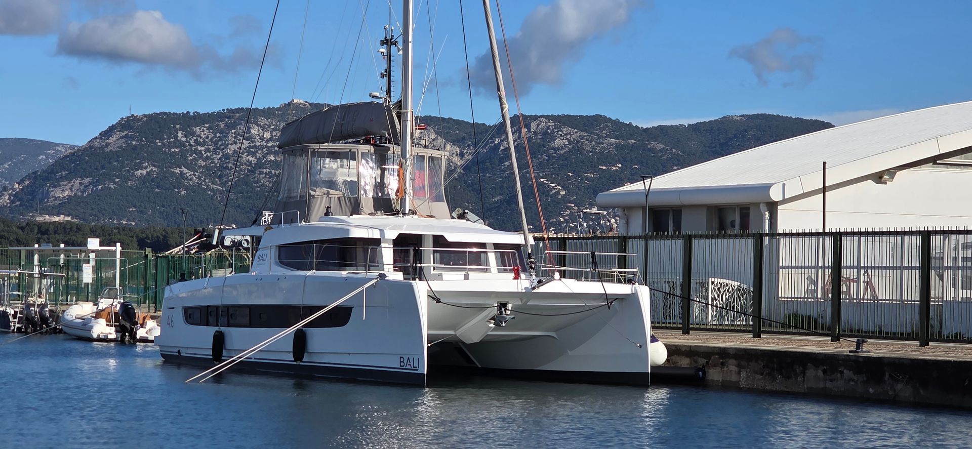 Un catamaran blanc, voiles déployées, sur un océan bleu sous un ciel dégagé.