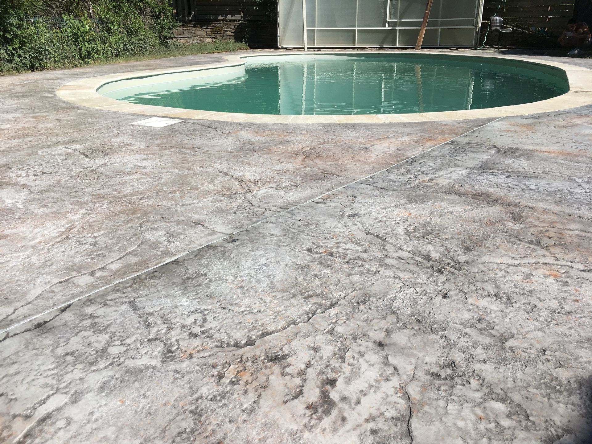 Piscine dans une cour arrière, jouxtant une terrasse en béton fissurée et une clôture.