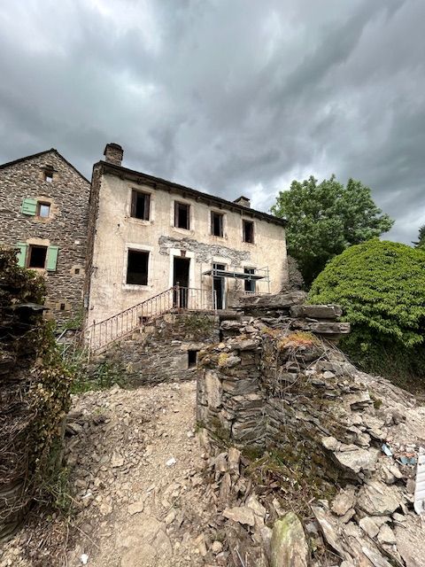 Vieille maison en pierre avec un chemin rocailleux abîmé sous un ciel nuageux, entourée d'arbres