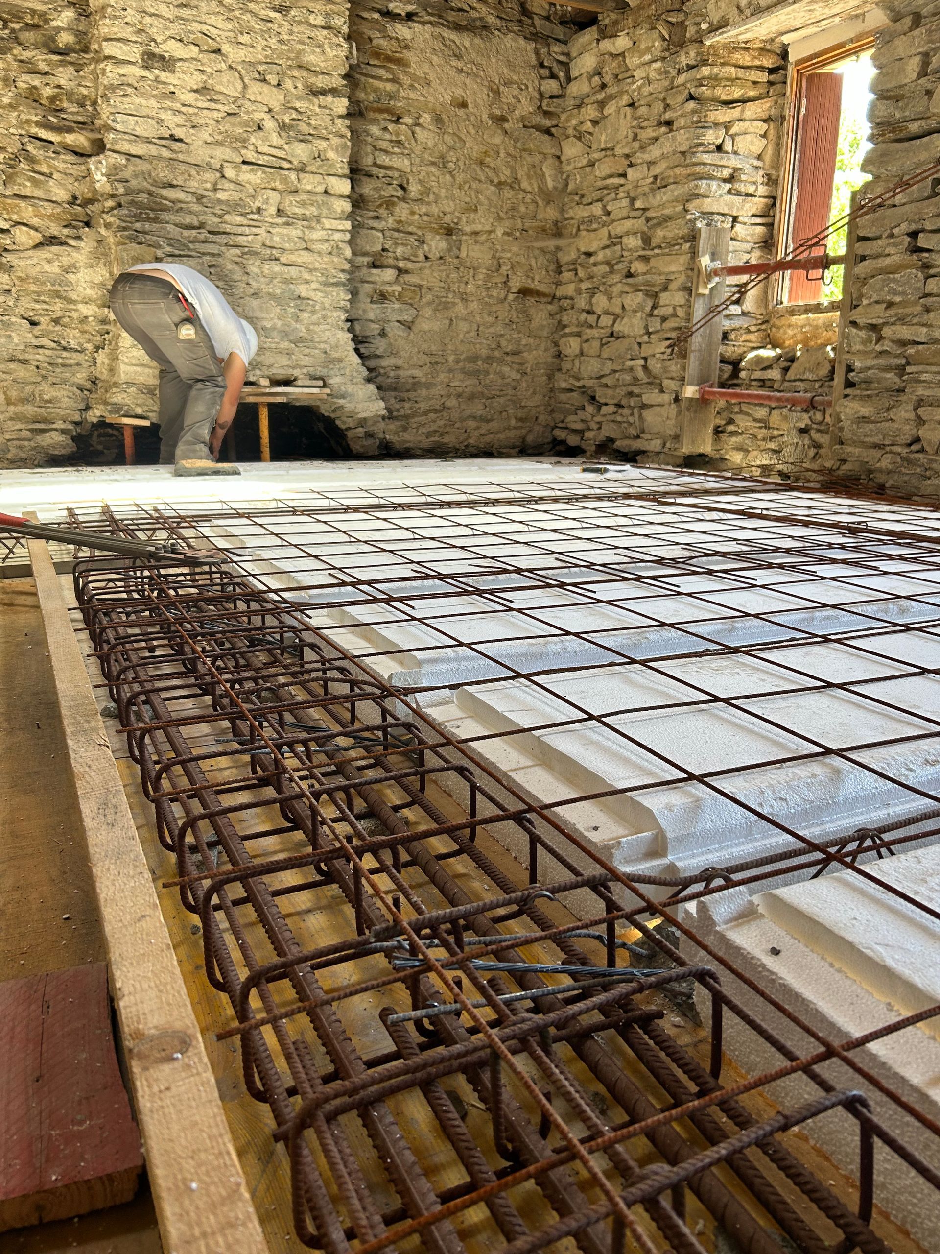 Un ouvrier penché sur des barres d'armature en acier dans une pièce aux murs de pierre en cours de rénovation