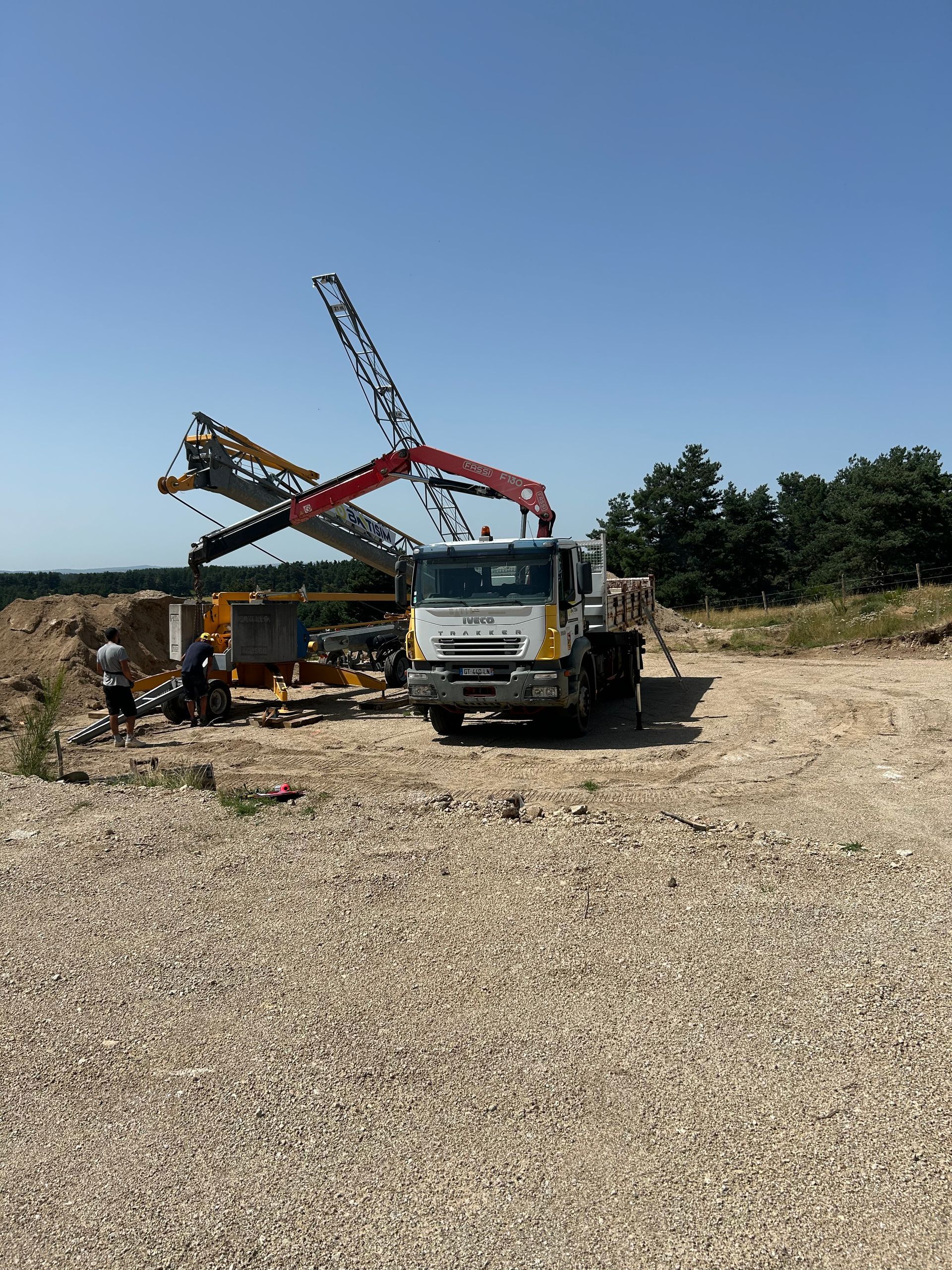 Des engins de chantier déchargent des copeaux de bois dans un champ sous un ciel bleu dégagé.