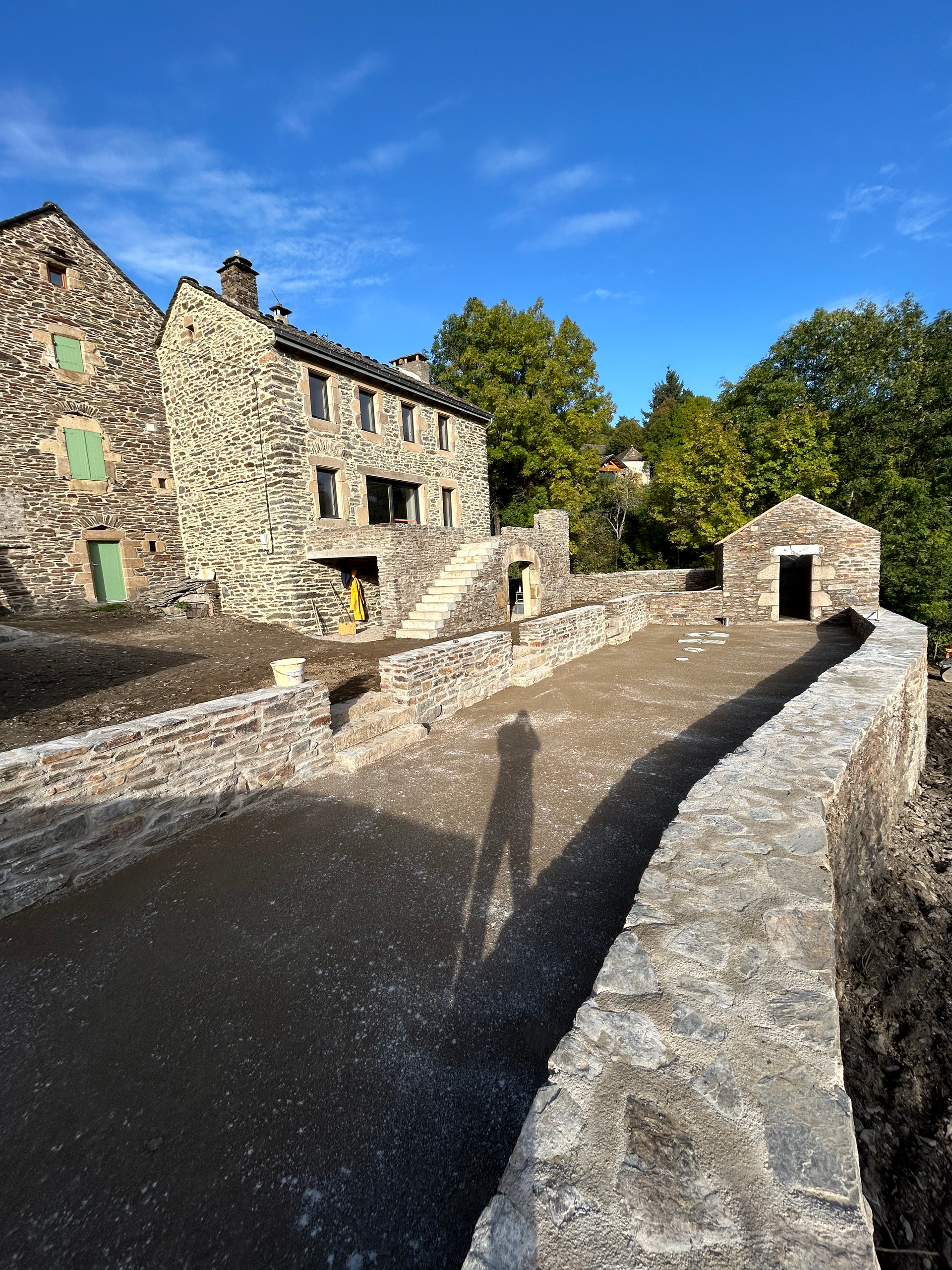 Bâtiments en pierre et murs voûtés dans une cour ensoleillée avec un chemin ombragé sous un ciel bleu