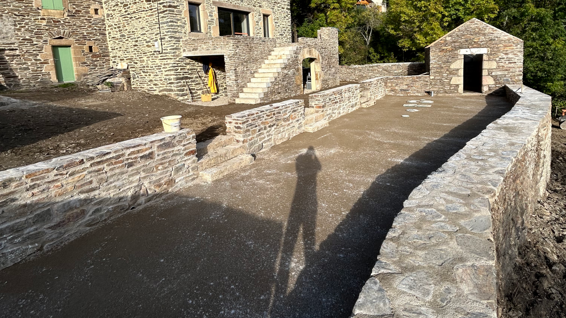 Cour en pierre avec une longue ombre, encadrée par de vieux bâtiments en pierre et baignée d'une lumière solaire éclatante.