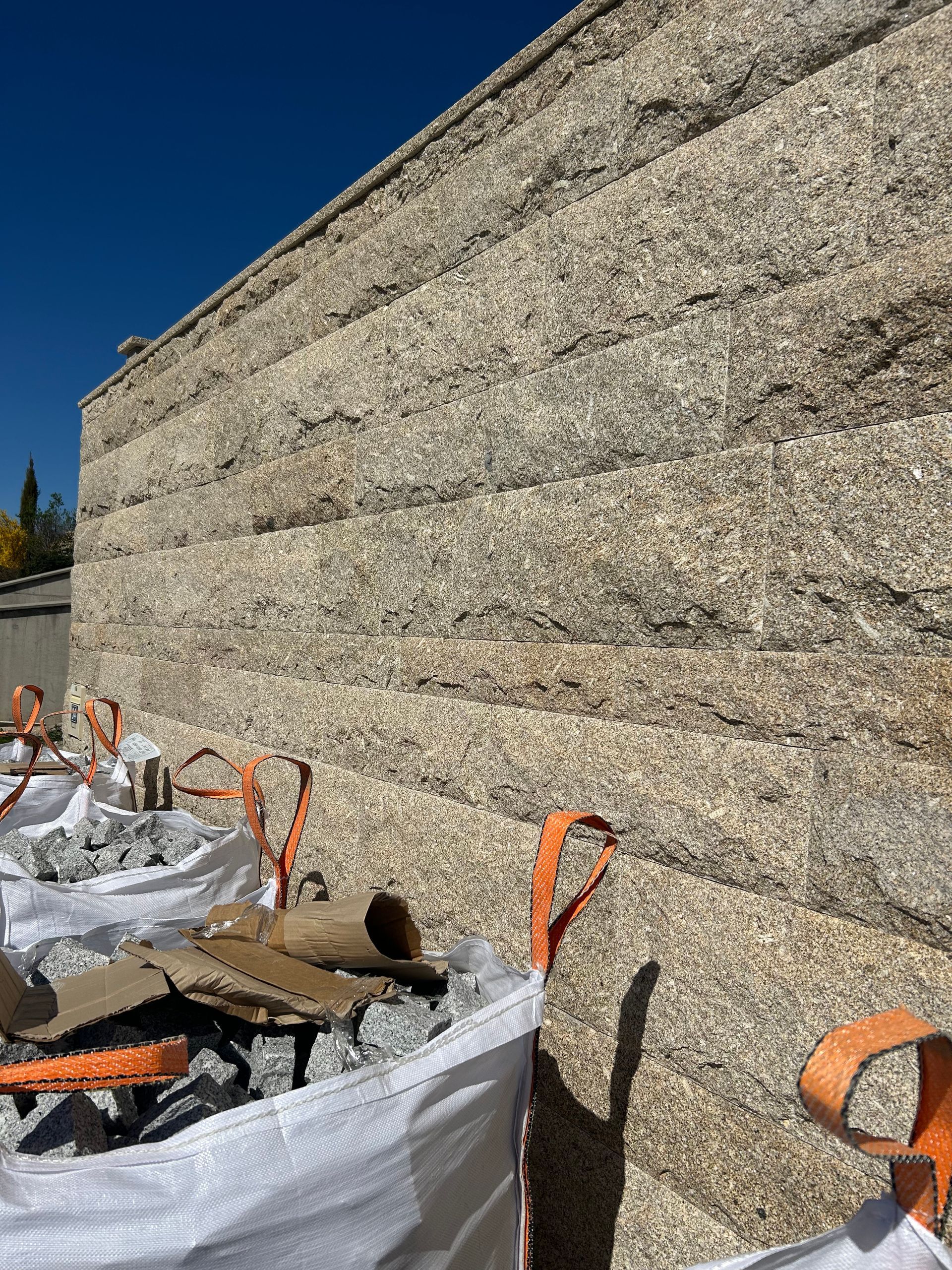 De grosses bottes de foin empilées, maintenues par des sangles orange, sous un ciel bleu clair.