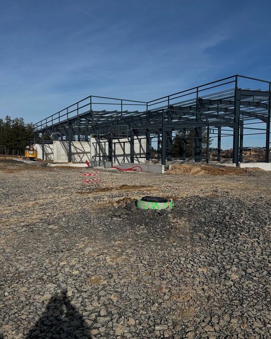 Une structure métallique en construction sur un terrain recouvert de gravier, sous un ciel bleu azur.