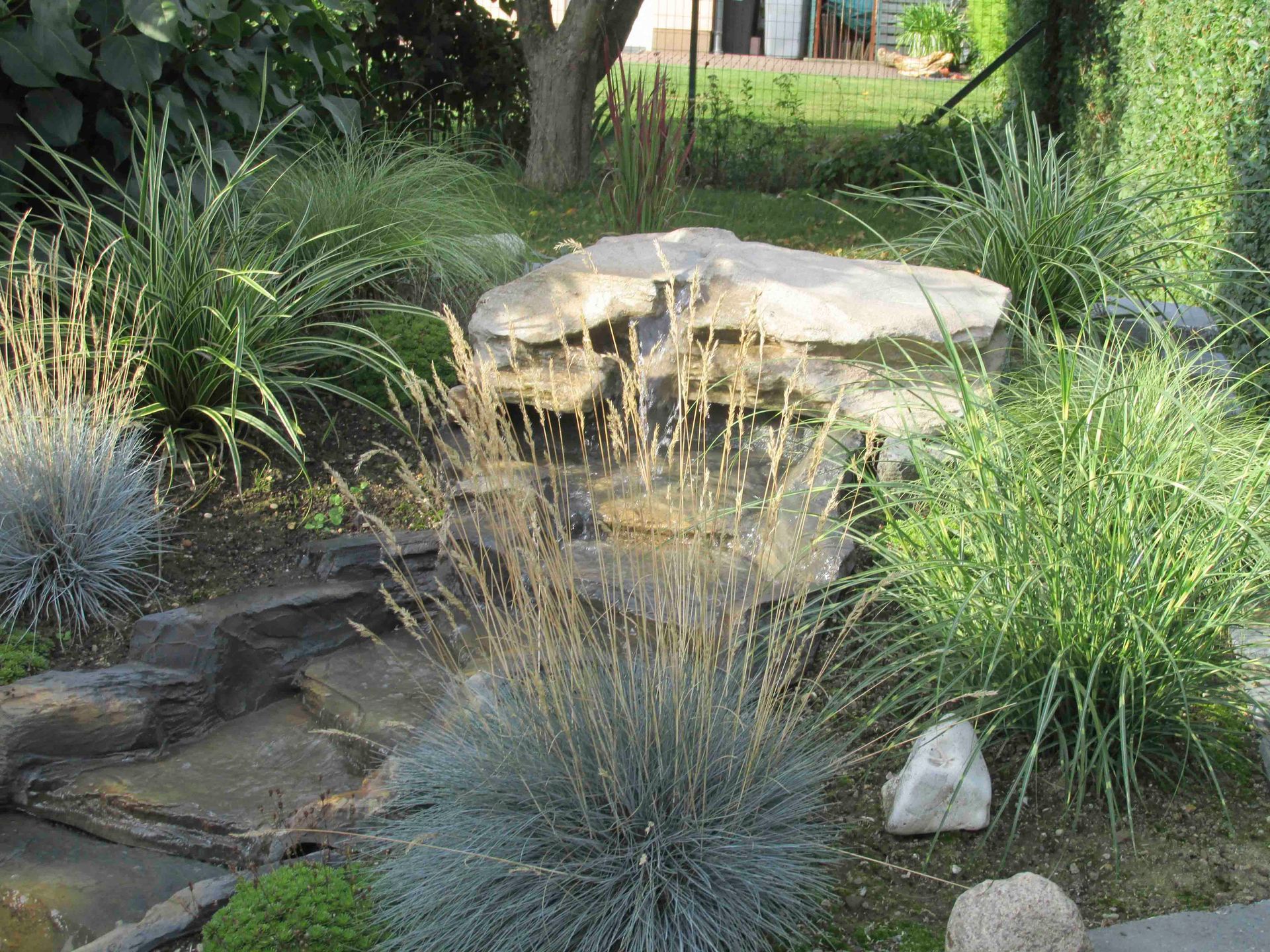 ein Wasserfall in einem Garten umgeben von Gras und Felsen