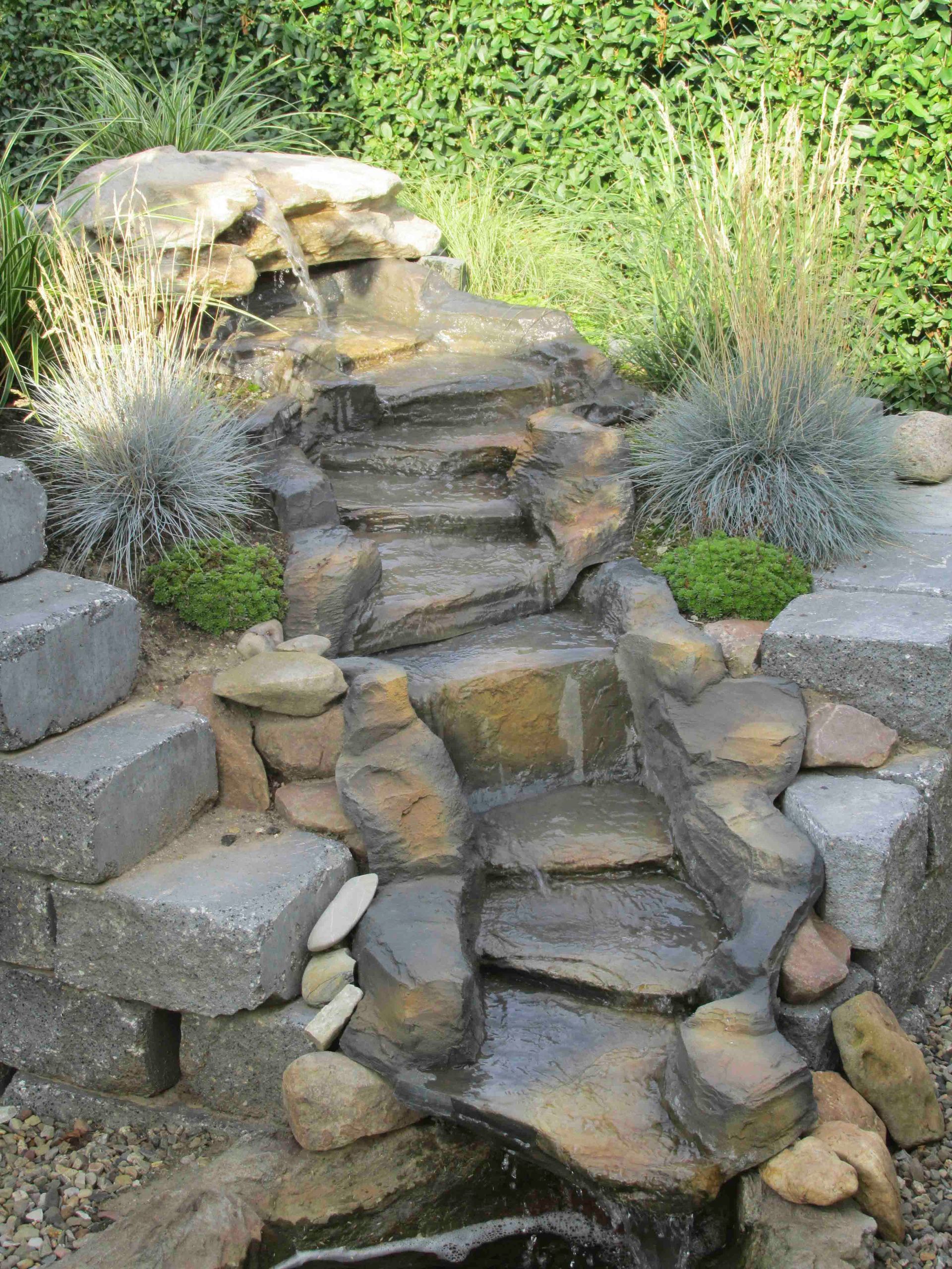 ein Wasserfall in einem Garten mit Steinen und Gras