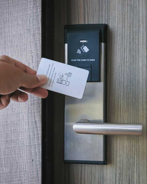 Mano sosteniendo una tarjeta llave blanca cerca de la cerradura de la puerta de un hotel.