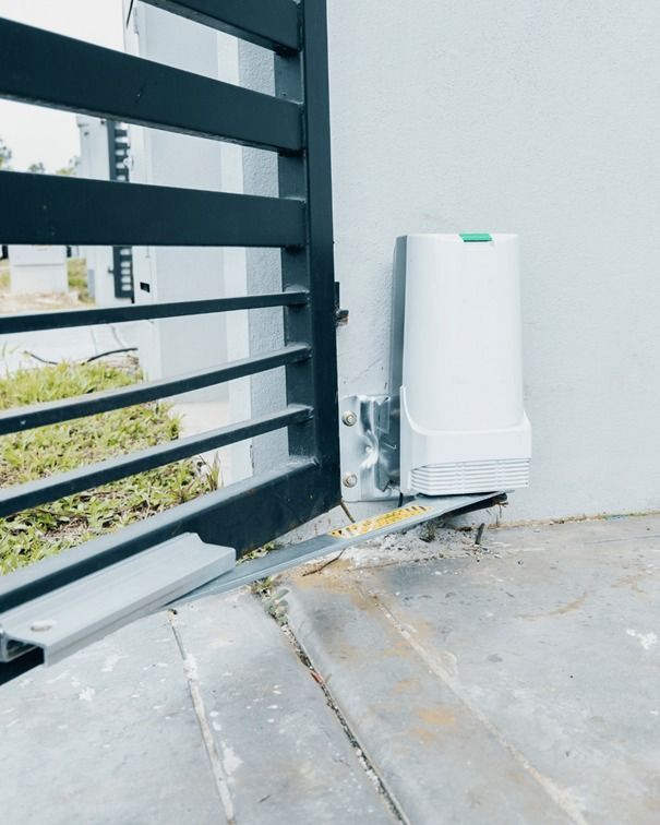 Abridor de puerta automático unido a una puerta de metal negra y una pared blanca, en exteriores.