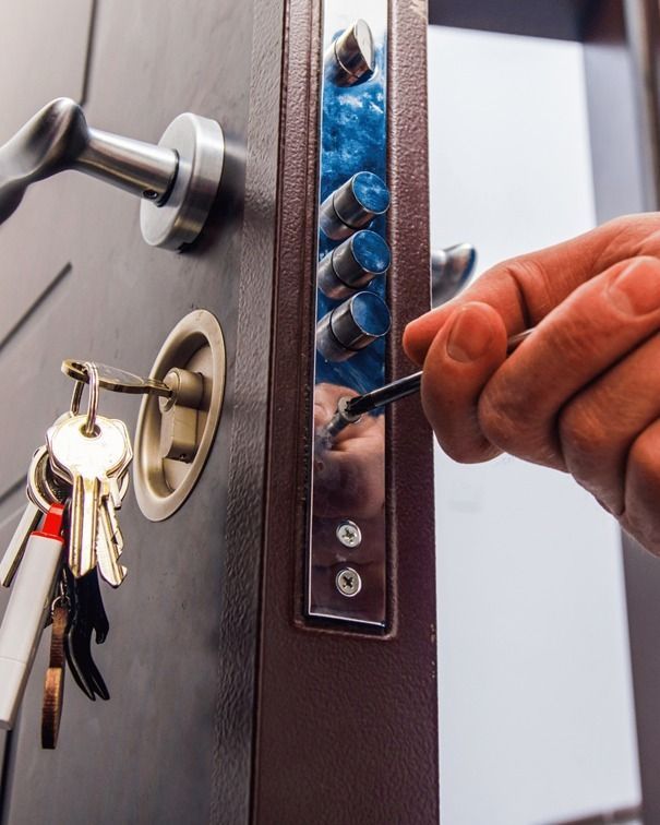 Persona usando un destornillador en la cerradura de una puerta. Hay un llavero con llaves en la cerradura.
