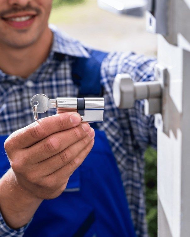 Cerrajero sosteniendo una cerradura con una llave, sonriendo mientras trabaja en una puerta.