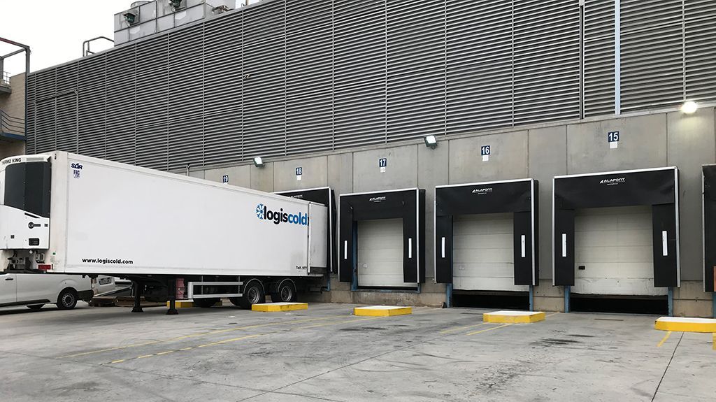 Semirremolque en un muelle de carga con varias bahías abiertas. Blanco y negro, exterior.