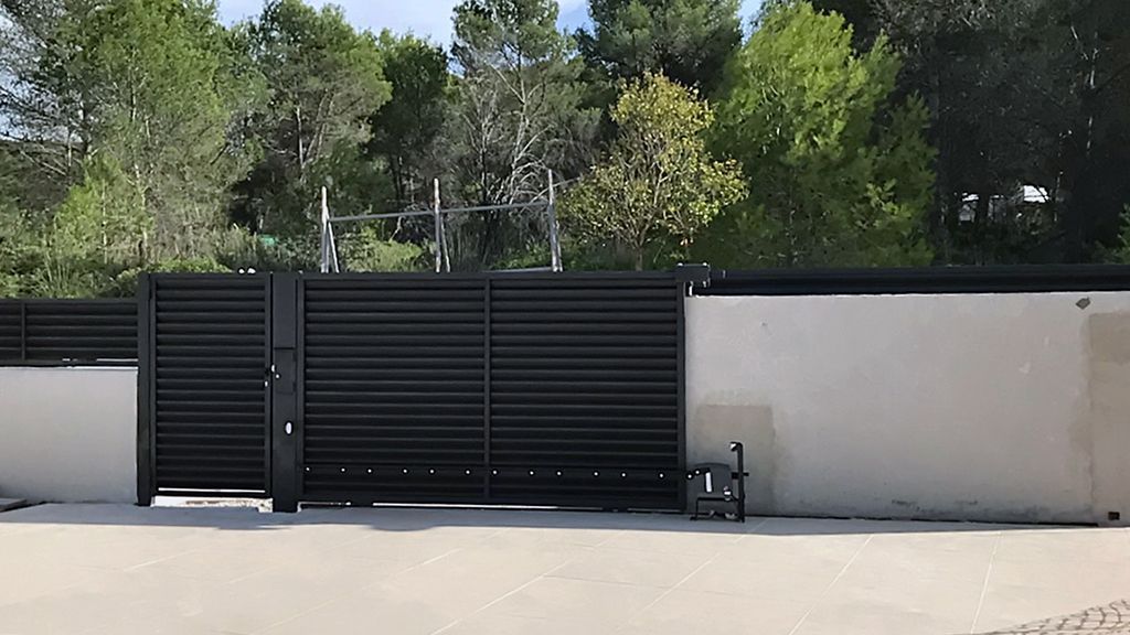 Puerta de metal negro que se abre deslizándose sobre un camino de entrada de concreto, revelando árboles.