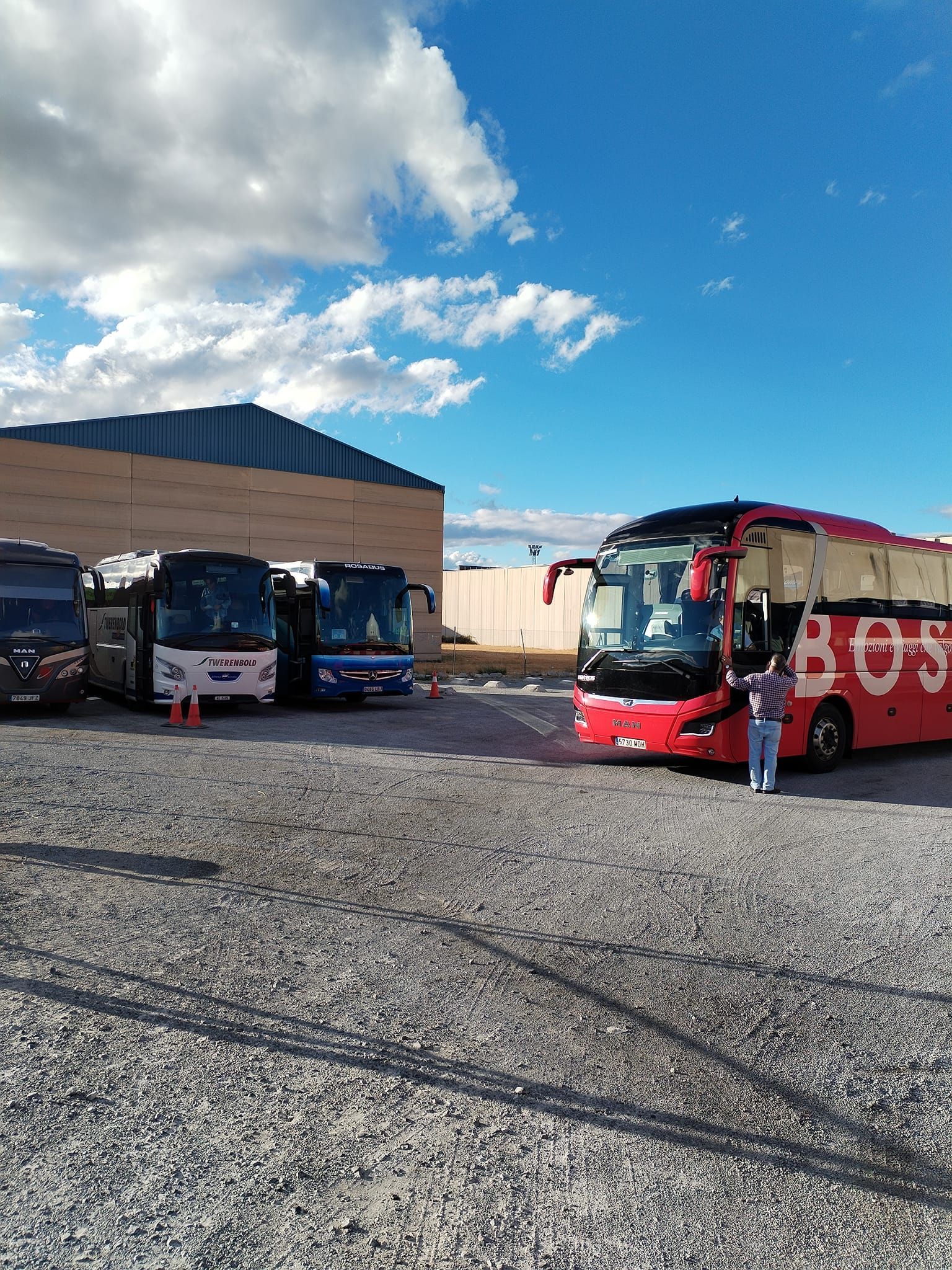 Un grupo de autobuses están estacionados en un estacionamiento de grava.