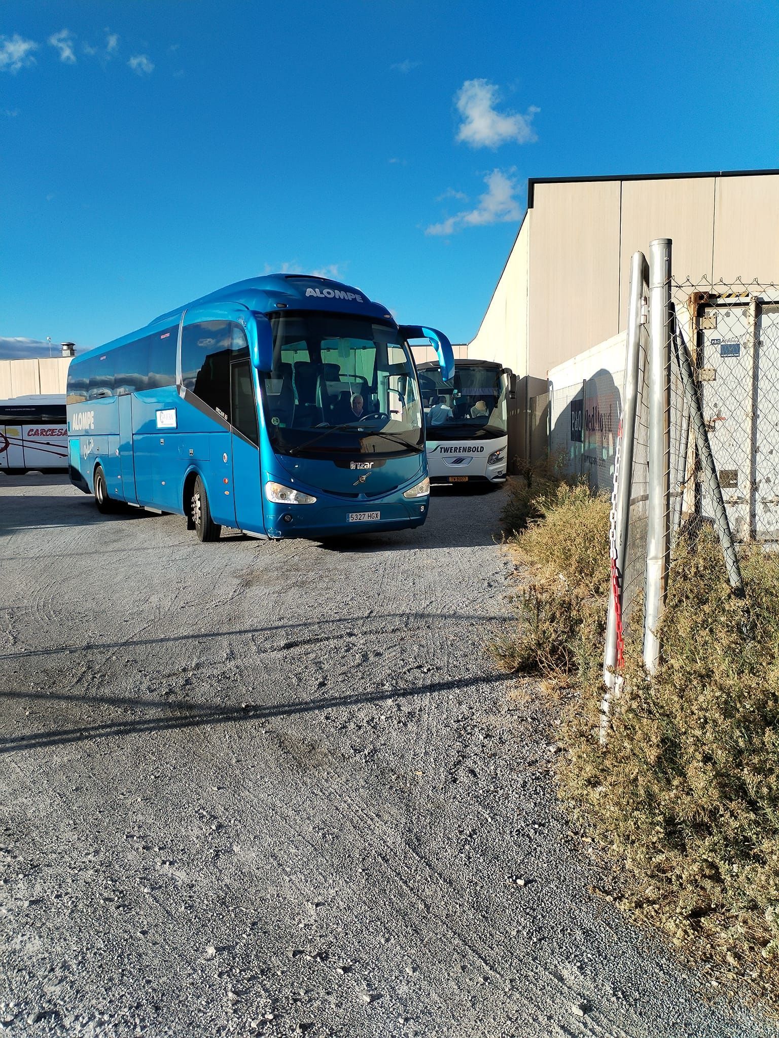 Un autobús azul está estacionado en un estacionamiento de grava frente a un edificio.
