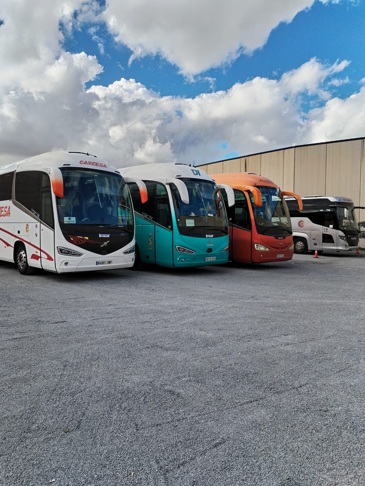 Una fila de autobuses están estacionados en un estacionamiento de grava.